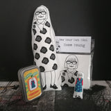 A Selection of gifts featuring an illustration of Esme Young including a black and white fabric doll, a mini doll and keepsake tin and a craft kit.