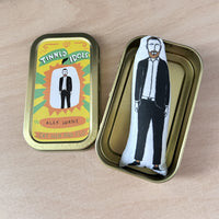 Mini fabric doll featuring an illustration of Alex Horne. The Alex doll lays in a tin beside a decorative tin lid.
