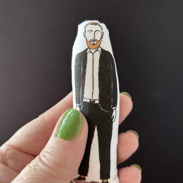 Mini fabric doll featuring an illustration of Alex Horne.  The doll is held in a hand.