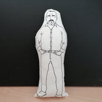Black and white screen printed fabric doll cushion featuring The Great British Bake Off and judge, Paul Hollywood. Stands against a black background on a light wood table.