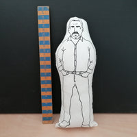 Black and white screen printed fabric doll cushion featuring The Great British Bake Off and judge, Paul Hollywood. To left is a wooden ruler. Stands against a black background on a light wood table.