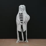 Black and white screen printed fabric doll cushion featuring The Great British Bake Off and judge, Prue Leith. Stands against a black background on a light wood table.