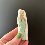 Mini illustrated fabric doll of Ted Lasso star Hannah Waddingham held up against a dark backdrop..