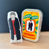 Mini fabric collectible doll and keepsake tin featuring an illustration of actor and comedian, Kathy Burke. On a wooden surface.