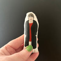 Mini fabric collectible doll featuring an illustration of actor and comedian, Kathy Burke. Held up against a dark backdrop to show the tiny size.