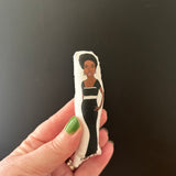 Mini fabric collectible doll featuring an illustration of singer songwriter, Nina Simone. Held up against a dark backdrop to show the tiny size.