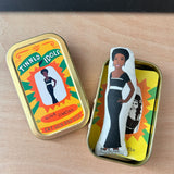 Mini fabric collectible doll and keepsake tin featuring an illustration of singer songwriter, Nina Simone. On a wooden surface.