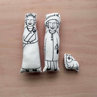 Black and white fabric Queen Elizabeth II dolls and corgi on a wooden surface
