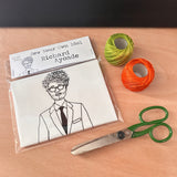 Sew Your Own Richard Ayoade doll cushion craft kit. On a wooden surface with craft supplies.