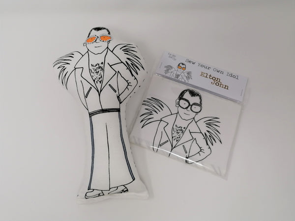 Black and white screen printed fabric doll of Elton John beside a craft sewing kit on a white background.