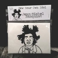 A sew your own Basquiat doll craft kit on a dark backdrop.