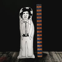 Black and white screen printed fabric doll featuring an illustration of artist Basquiat. Beside the doll is a wooden ruler to show scale. All against a black wall.