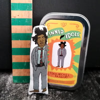Mini fabric art doll and gift tin of New York artist Jean-Michel Basquiat. A wooden ruler stands beside them to indicate size.