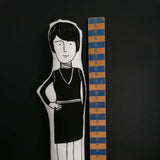 Black and white fabric doll beside a wooden ruler for scale against a black background.