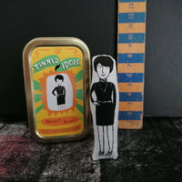 A mini fabric doll and tin of artist Bridget Riley beside a wooden ruler for scale.