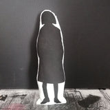 Reverse of a black and white screen printed cushion doll featuring an illustration of Esme Young. Set against a black background and standing on a textured surface.