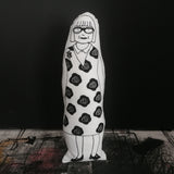 Black and white screen printed cushion doll featuring an illustration of Esme Young. Set against a black background  and standing on a textured surface.