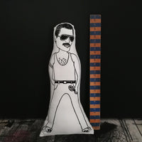Black and white illustrated doll cushion of Freddie Mercury. Against a black wall beside a vintage wooden ruler for scale.