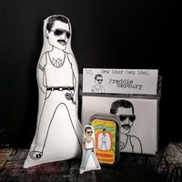 A selection of gifts of Freddie Mercury. An illustrated black and white fabric doll, a mini fabric doll and tin, and a craft kit.