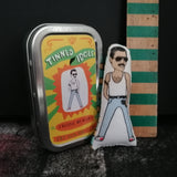 Mini fabric art doll and gift tin of Queen front man Freddie Mercury set against a dark background.