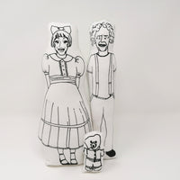 Black and white screen printed dolls of Grayson Perry, his alter ego Claire and his teddy bear, Alan measles against a white background.