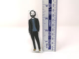 MIni fabric Keanu Reeves doll stood next to a ruler on a white background