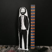 A black and white screen printed fabric doll featuring an illustration of Keanu Reeves, stood beside a wooden ruler to indicate scale.