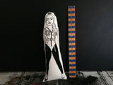 A black and white fabric doll of Madonna beside a wooden ruler.