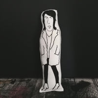 Black and screen printed cushion doll of Might Boosh creator and star, Noel Fielding. Stood against a black background.