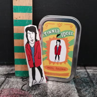 A mini fabric art doll of The Mighty Boosh star, Noel Fielding. It is stood between a wooden ruler to indicate scale and a keepsake gift tin.