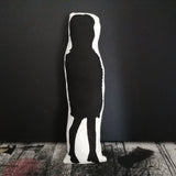 The reverse of a fabric doll featuring a silhouette of Noel Fielding. Against a dark background.