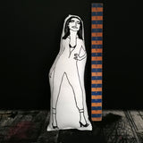 Black and white screen printed fabric doll of PJ Harvey. The doll is leant against a black wall beside a wooden ruler for scale.