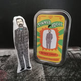 A mini fabric doll beside a keepsake tin with sticker detail on the lid. The doll features an illustration of Patrick Grant.