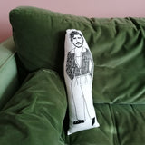 A green sofa against a pink wall. On the sofa is a black and white illustrated cushion featuring Pedro Pascal.