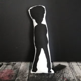 Silhouette design reverse of a fabric Robert Smith doll set against a black wall.
