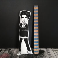 Black and white fabric doll of Robert Smith beside a wooden ruler against a black wall.