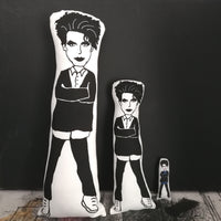 Three different sized Robert Smith fabric dolls stood in siize order against a black wall.
