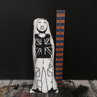 Black and white fabric screen printed cushion doll featuring an illustration of Stormzy, beside a wooden ruler for scale.