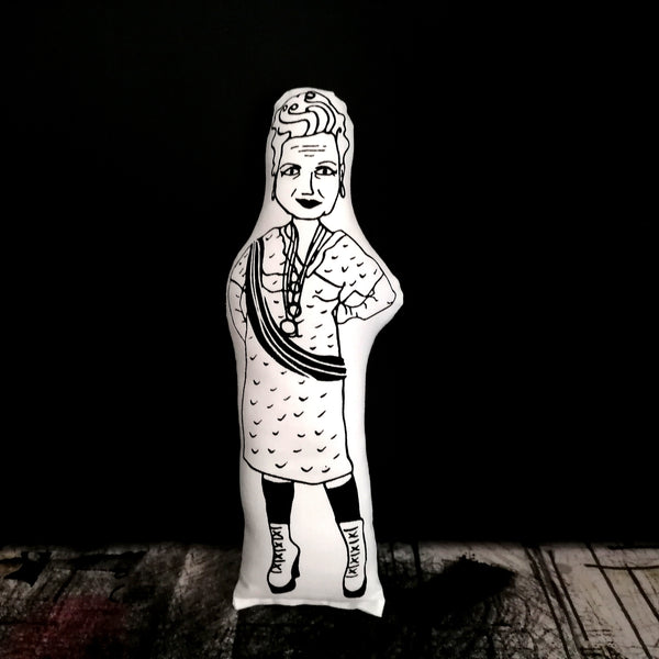 Monochrome screen printed fabric doll of fashion designer Vivienne Westwood set against a black wall and textured surface.