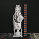 Black and white screen printed fabric doll of Vivienne Westwood beside a wooden ruler against a dark backdrop.
