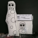 A black and white screen printed fabric doll beside a craft kit against a black background. 