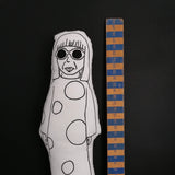 Close up of a black and white fabric doll of Yayoi Kusama next to a wooden ruler.