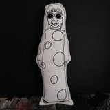 A black and white screen printed fabric doll of Yayoi Kusama against a black backdrop.
