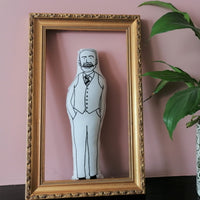 Gareth Southgate fabric doll on a mantlepiece in empty gilt frame beside a house plant