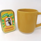 Mini doll of Jarvis Cocker in a tin beside a yellow mug for scale