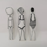 Reverse of three screen printed fabric swimmer dolls made from a craft kit. Swimmers are wearing swim hats and a bikini and swimsuits.