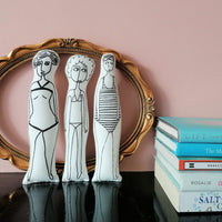 Set of three swimmer fabric dolls made from a sew your own swimmer craft kit, displayed on a mantelpiece beside sea themed books.