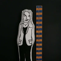 Black and white fabric doll of Tracey Emin beside a wooden ruler.